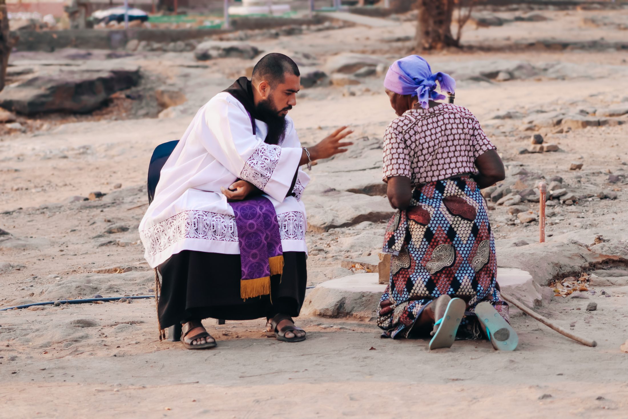 Friar kneeling and talking to someone on the ground